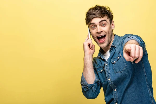 Cheerful Young Man Pointing Finger Camera While Talking Smartphone Yellow — Stock Photo, Image