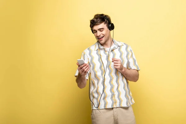 Cheerful Young Man Listening Music Headphones Using Smartphone Yellow Background — Stock Photo, Image