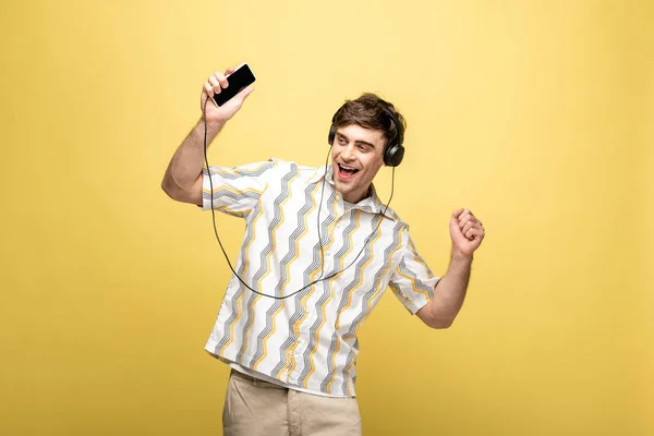 黄色の背景にヘッドフォンやスマートフォンで音楽を聴きながら踊る陽気な若者 — ストック写真