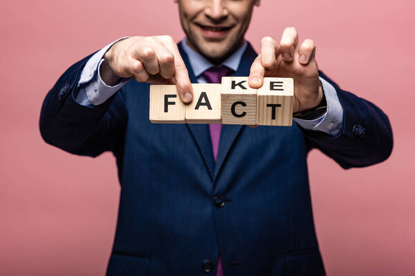 частичный взгляд бизнесмена, держащего деревянные кубики с поддельными буквами на розовом фоне
