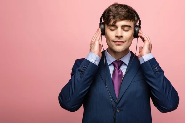 沉思的微笑男子在耳机里听音乐 在粉红色背景上闭上眼睛 — 图库照片