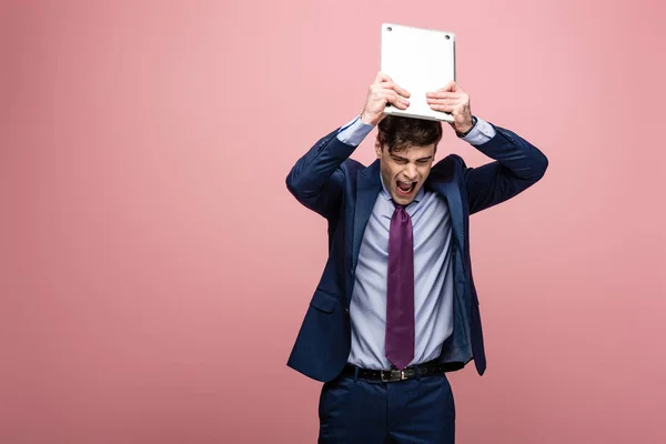 Сердитий Бізнесмен Сварки Тримаючи Ноутбук Над Головою Рожевому Фоні — стокове фото