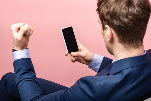 ピンクに隔離された空白の画面でスマートフォンを保持しながら拳を示すビジネスマンのトリミングビュー — ストック写真
