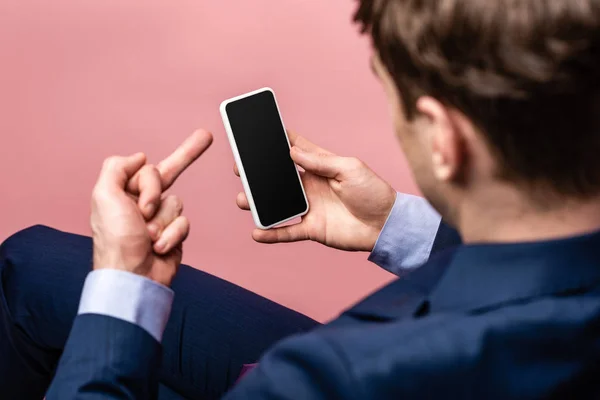 ピンクに隔離された空白の画面でスマートフォンを保持しながら中指を示すビジネスマンの部分的なビュー — ストック写真