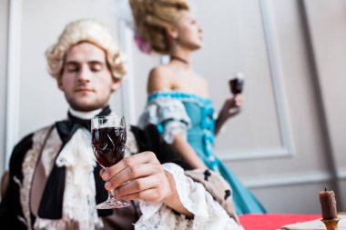 selective focus of victorian man in wig holding glass wine near pompous woman  clipart
