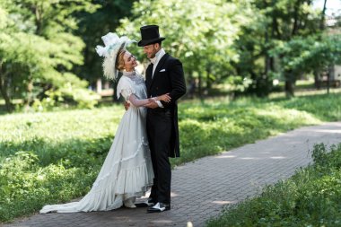 handsome victorian man and attractive woman looking at each other while standing outside  clipart