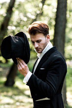 handsome aristocratic man holding hat while standing in suit 