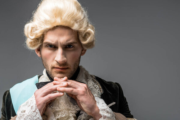 серьезный викторианский джентльмен в парике смотрит на камеру, изолированную на сером
