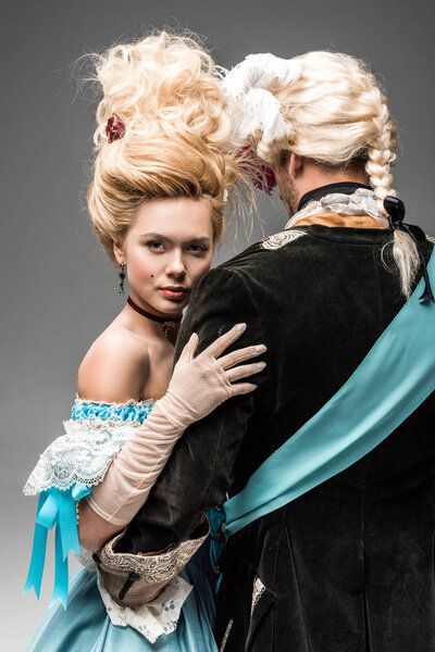 back view of man hugging attractive victorian woman in wig on grey