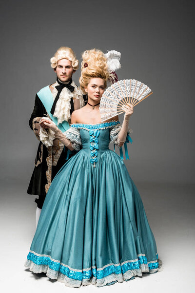 Молодая викторианка с веером, держащимся за руки, стоя с джентльменом на сером
