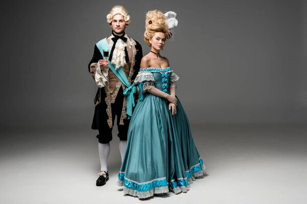 Красивый джентльмен держит бокал вина рядом с Викторианской женщиной на серой
 