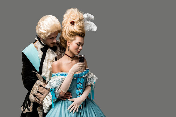 Красивый джентльмен смотрит на красивую Викторианку с бокалом вина, изолированным на сером
 