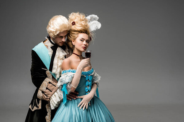 Красивый джентльмен смотрит на красивую викторианскую женщину с бокалом вина на сером
 