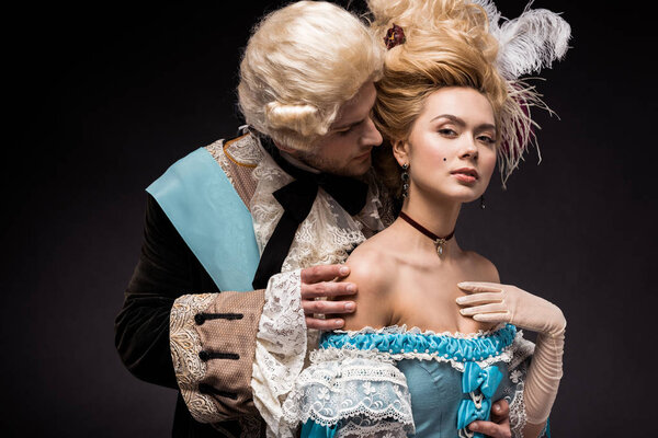 handsome victorian man looking at young woman in wig on black 