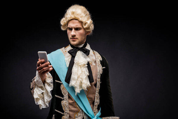 handsome victorian man in wig looking at smartphone on black 