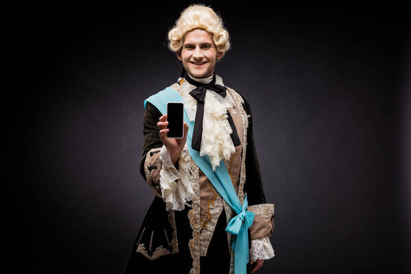 красивый викторианский мужчина в парике держит смартфон с чистым экраном на черном
 