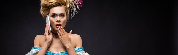 панорамный снимок удивленной викторианки разговаривающей по смартфону на черном
 