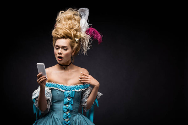 shocked young victorian woman in blue dress looking at smartphone on black 