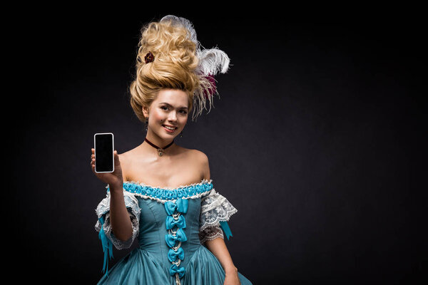 young victorian woman in blue dress holding smartphone with blank screen on black 