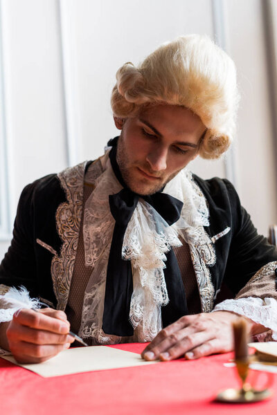 selective focus of handsome victorian man in wig writing letter 