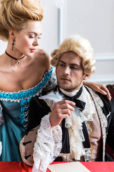 beautiful victorian woman standing near pompous man holding feather near paper 