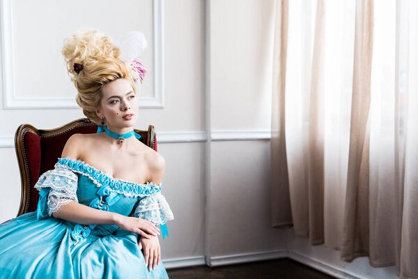 красивая молодая викторианка в синем платье сидит на антикварном стуле
 