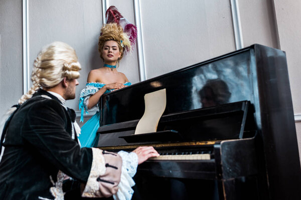селективное внимание женщины-викторианки, смотрящей на мужчину в парике, играющего на пианино
 