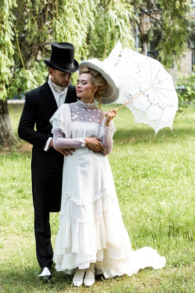 handsome victorian man standing with attractive woman holding umbrella