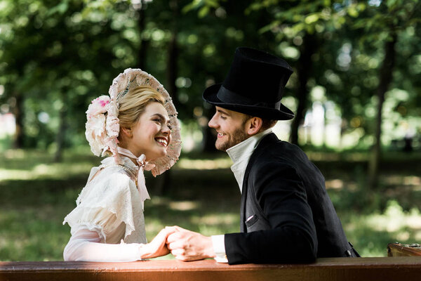 handsome aristocratic man holding hands with cheerful victorian woman in hat 