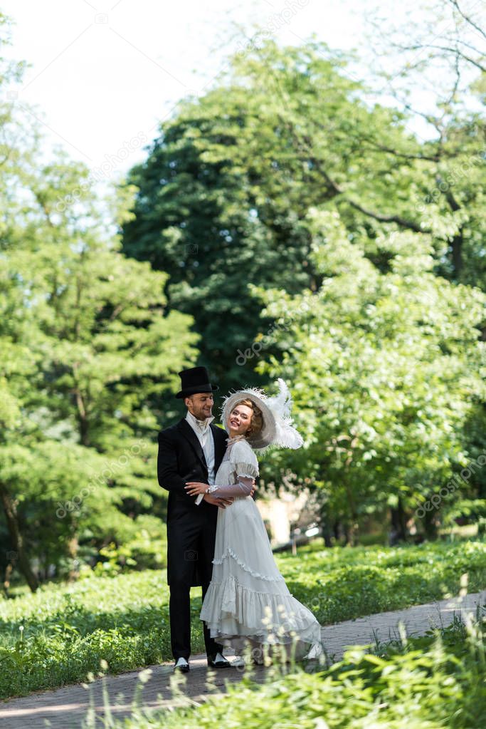 handsome victorian man looking at attractive woman in hat while standing outside 