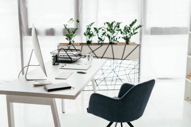 white table with computer, document tray, glass and notebook near office chair and flowerpot with plant clipart