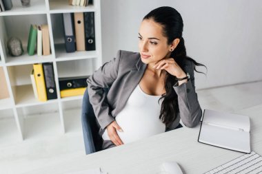 hamile kadın masanın arkasında oturan ve uzağa bakıyor 