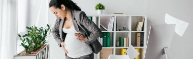 panoramic shot of exhausted pregnant woman standing in office and enduring pain clipart