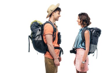 two young, smiling tourists with backpacks looking at each other isolated on white clipart