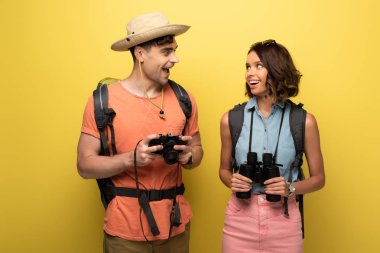 dürbün ve dijital kamera ile iki neşeli turist sarı arka planda birbirlerine bakıyor