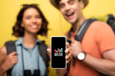 Kiev, Ukrayna - 3 Haziran 2019: Sarı arka planda gülümseyen adamın yanında dururken Deezer uygulamasıyla akıllı telefonu gösteren neşeli kadının seçici odağı.
