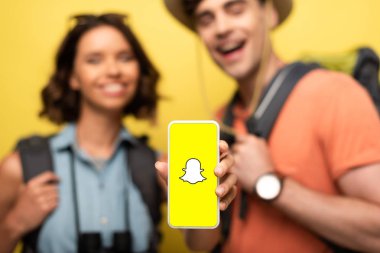 Kiev, Ukrayna - 3 Haziran 2019: Sarı arka planda gülümseyen adamın yanında dururken Snapchat uygulaması yla akıllı telefonu tutan neşeli kadının seçici odağı.