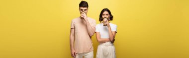 panoramic shot of young man and woman drinking coffee to go while looking at camera on yellow background clipart