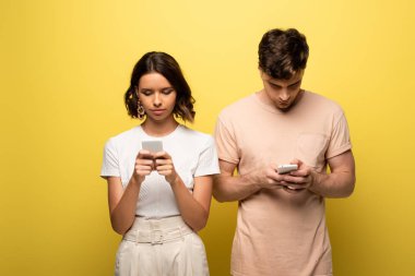 sarı arka planda akıllı telefonlar kullanarak özenli erkek ve kadın