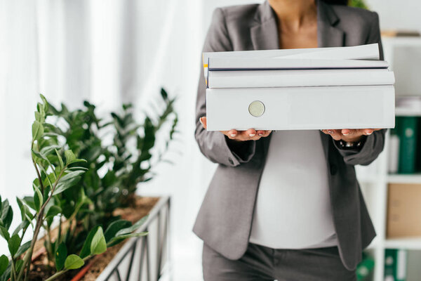cropped view of woman holding folders while standing near flowerpot with plants