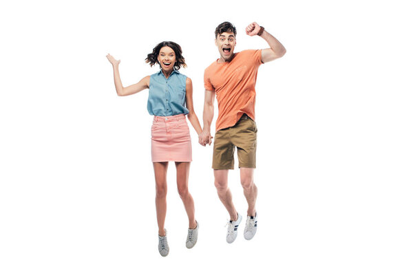 cheerful man and woman holding hands and jumping while looking at camera isolated on white