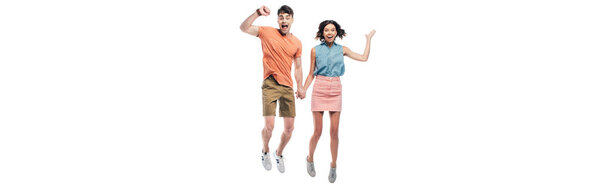 panoramic shot of happy man and woman holding hands and jumping while showing triumph gestures isolated on white