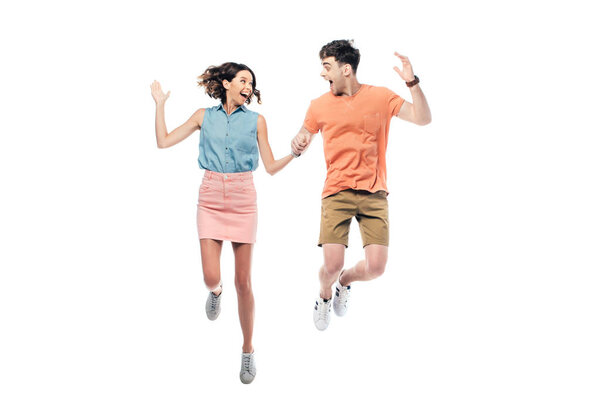 excited man and woman jumping while looking at each other isolated on white