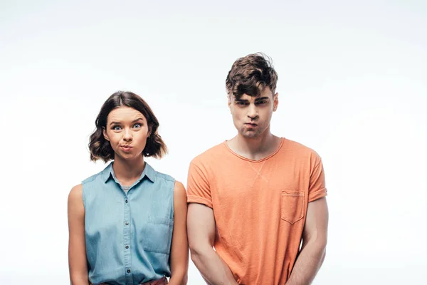 young, displeased man and woman looking at camera and grimacing on white background