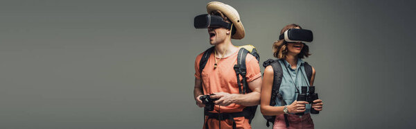 панорамный снимок двух молодых туристов в наушниках виртуальной реальности на сером фоне
