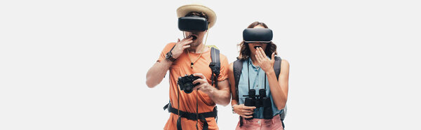 panoramic shot of two surprised tourists using virtual reality headsets isolated on grey