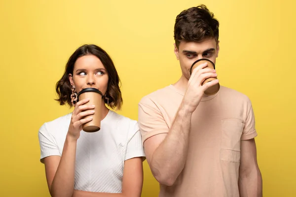 陽気な男女がコーヒーを飲んで 黄色の背景でお互いを見つめ合いながら行く — ストック写真