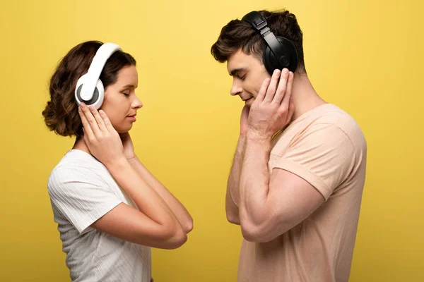 年轻的男人和女人在耳机听音乐与黄色背景闭上眼睛 — 图库照片