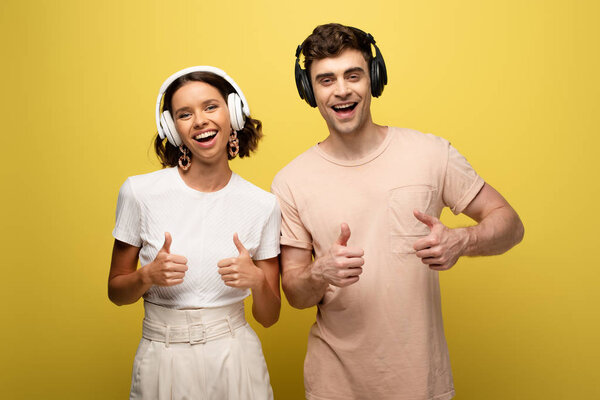 cheerful man and woman showing thumbs up while smiling at camera on yellow background