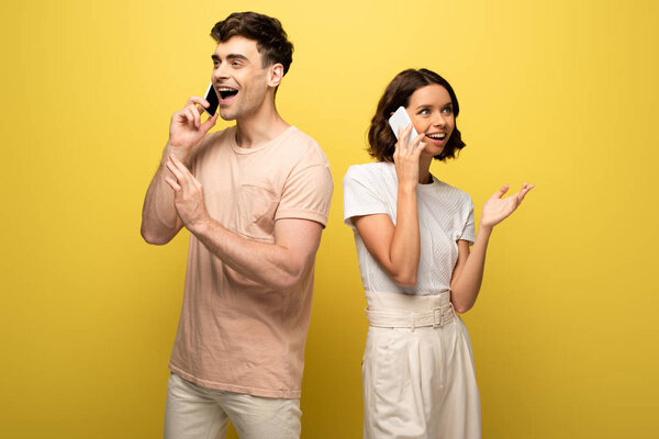 smiling man and woman talking on smartphones and looking away on yellow background